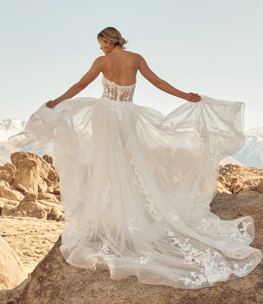 Braut steht mit Ihren Brautkleid auf einem Stein vor einem Gebirge.