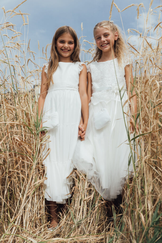 Zwei Mädchen in Kommunionkleidern in einem Getreidefeld. Weiße Kommunionkleider